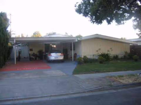 A single-story beige senior home with carport and parked car at front.