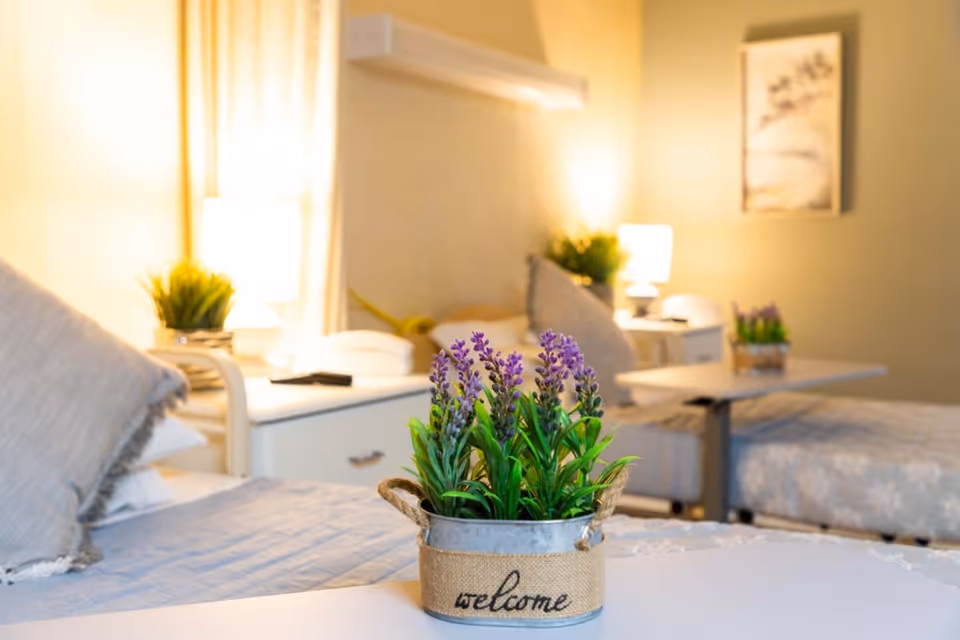 Two beds in a warmly lit bedroom with bedside tables and lamps and a small potted lavender in a "welcome" container on a table in the foreground.