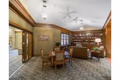 A cozy communal lounge with a table and chairs in the foreground, sofas and bookshelves along the back, and wood-paneled trim.
