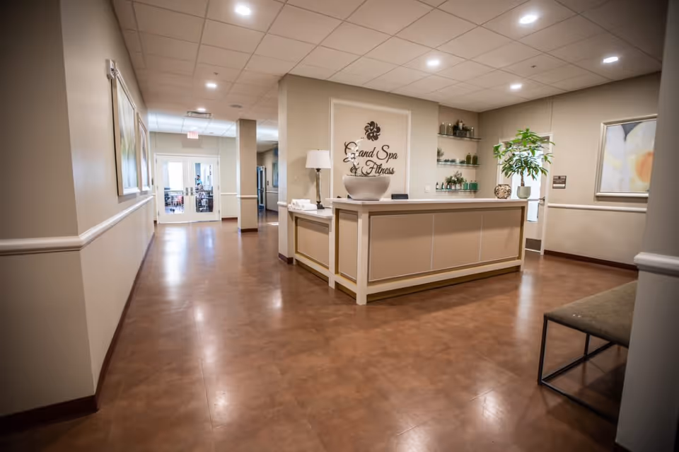 Reception area with a central desk labeled 'Grand Spa & Fitness' in a bright hallway of the senior living facility.