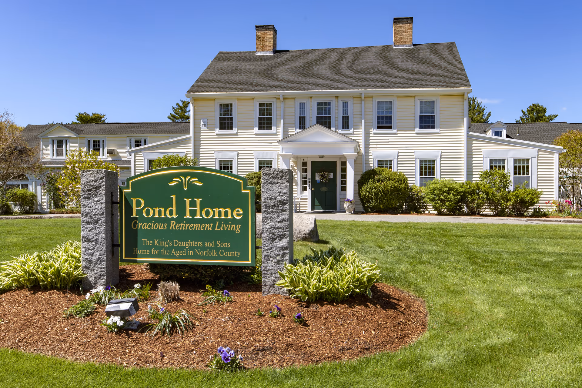 Front exterior of a yellow two-story retirement home with a green "Pond Home" sign on the lawn.