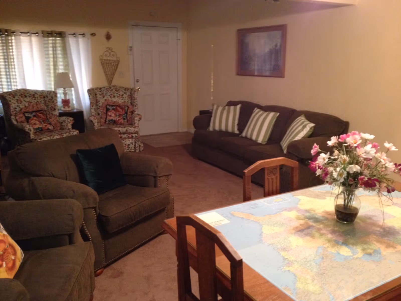 Cozy living room with sofas and armchairs, and a dining table with a map and vase of flowers in the foreground.