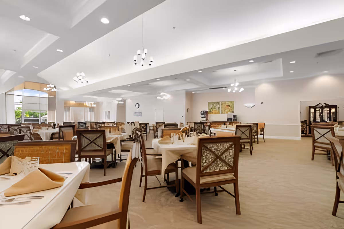 Spacious, well-lit dining room with multiple set tables and wooden chairs under recessed ceilings and chandeliers.