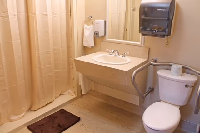 Accessible bathroom with a sink, toilet with grab bars, and a shower with a beige curtain.