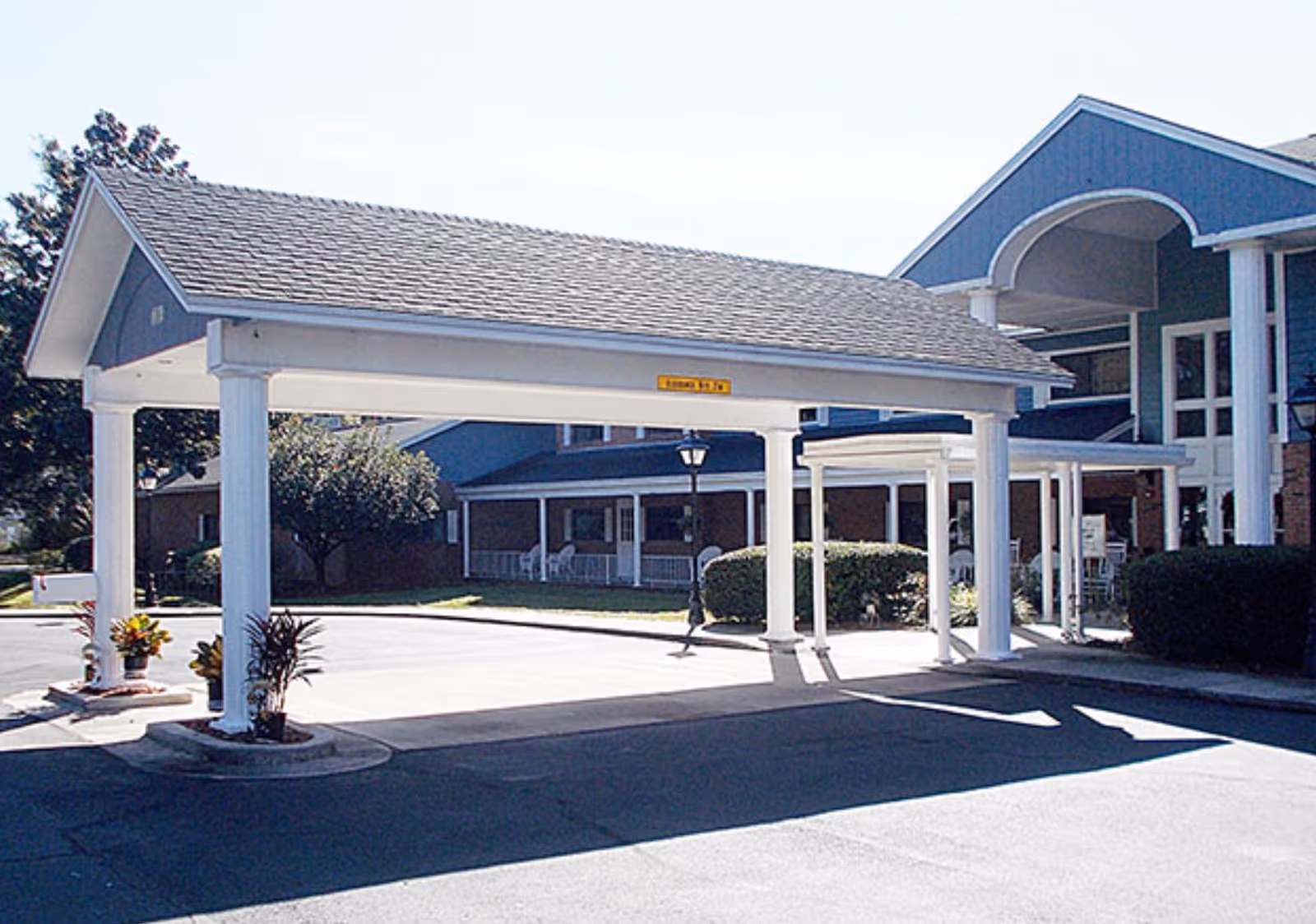 Covered entrance canopy and drive-up portico with white columns in front of a senior living building and landscaping.