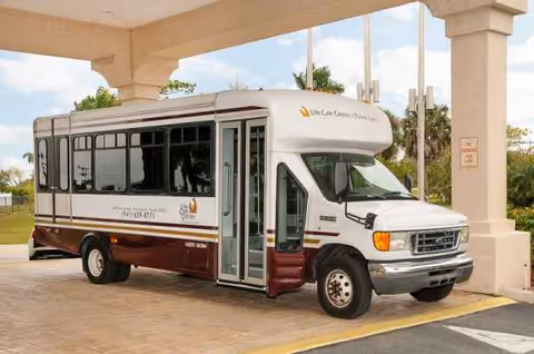 A white Life Care Center shuttle bus parked at the facility entrance under a covered drop-off.