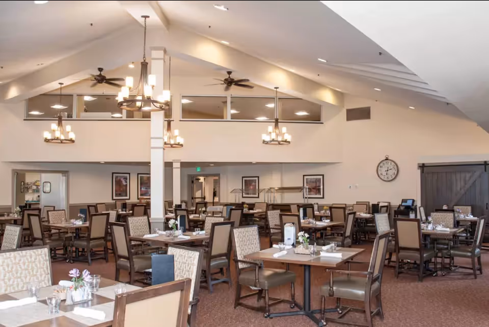 Spacious dining room with multiple set tables and chairs under a vaulted ceiling with chandeliers.