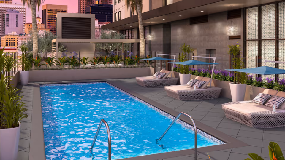 Rooftop swimming pool with lounge chairs, umbrellas and potted plants against a city skyline.