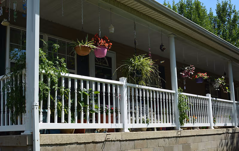 Front porch with a white railing and multiple hanging and potted plants.