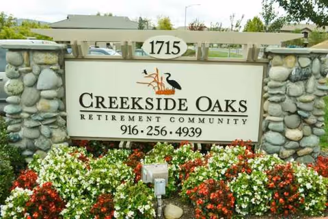 Exterior stone sign for Creekside Oaks Retirement Community with colorful flowers in front.