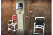 Two shower chairs with armrests and back support placed inside a tiled shower area with a wall-mounted soap dispenser and showerhead visible.