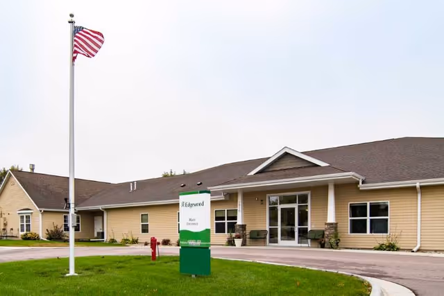 Front entrance of a single-story assisted living building with a flagpole, a green Edgewood sign, and a circular driveway.