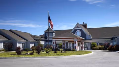Front exterior of The Gardens at Wapakoneta with a circular driveway and American flag.