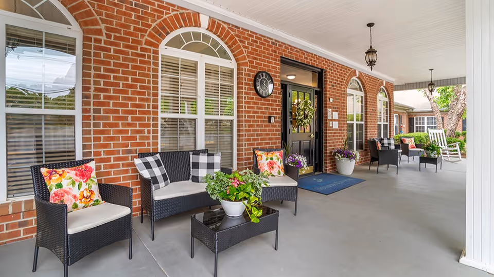 Covered brick front porch with wicker chairs and sofas, potted plants, and a black entrance door.