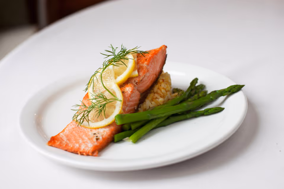 Plated salmon fillet topped with lemon slices and dill, served with rice and asparagus on a white plate.