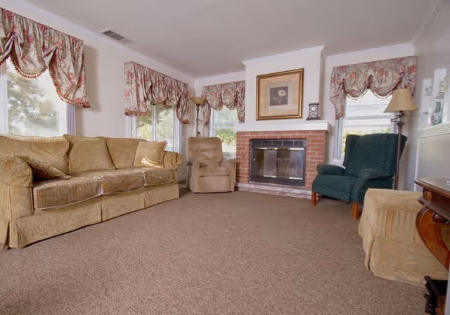 Cozy living room with a sofa and armchairs arranged around a brick fireplace beneath patterned window valances.
