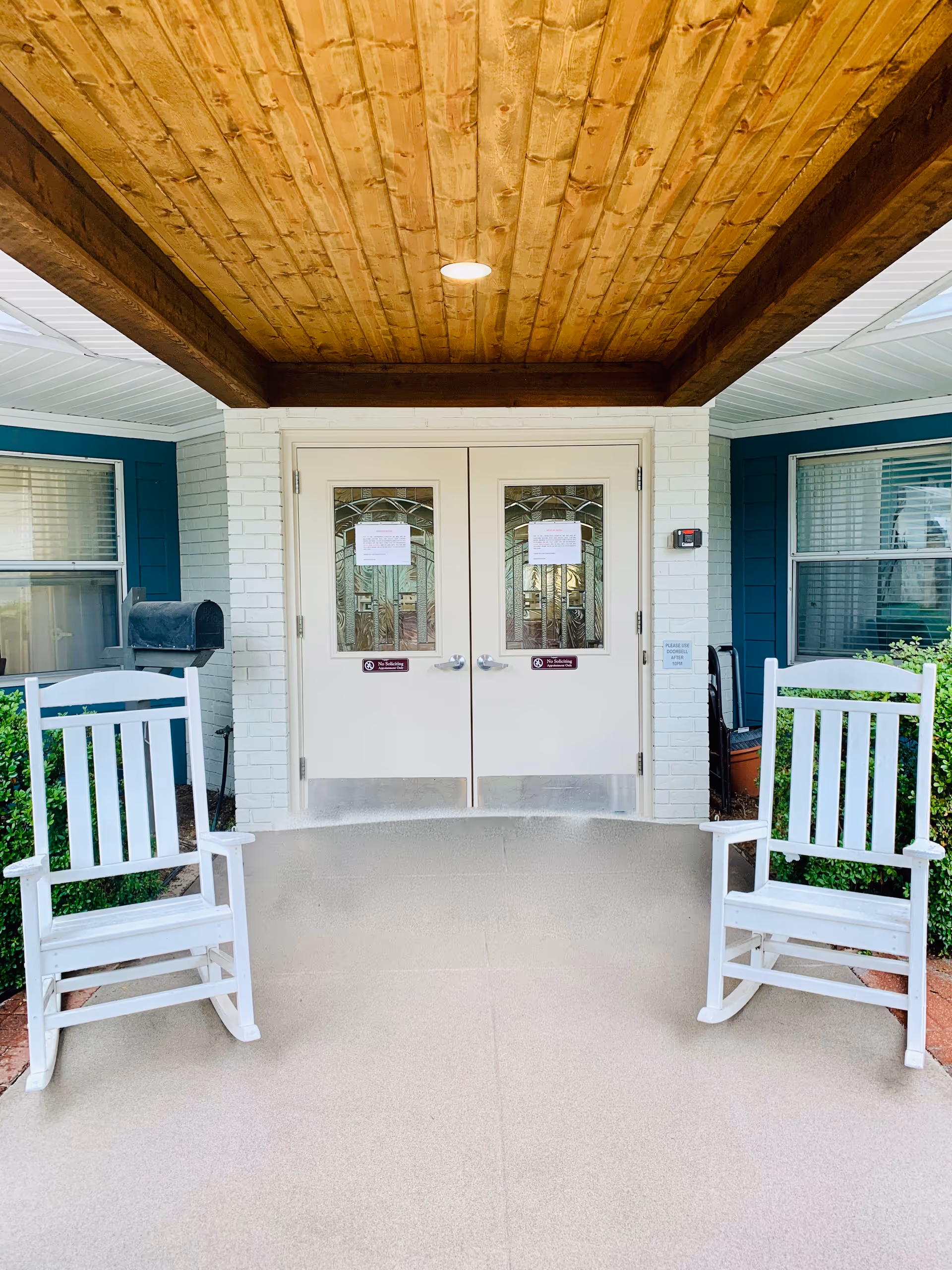 Covered entrance with double glass doors and two white rocking chairs on a porch.