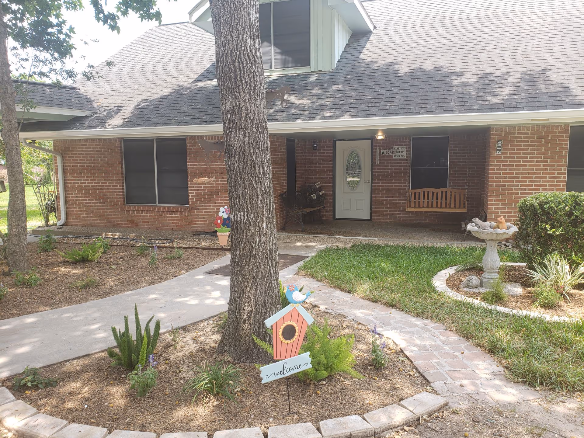 Brick one-story senior living facility front with porch, walkway, and garden decorations.