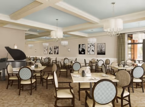 Bright, elegant dining room with multiple round tables and upholstered chairs, chandeliers, framed artwork on the walls, and a baby grand piano.