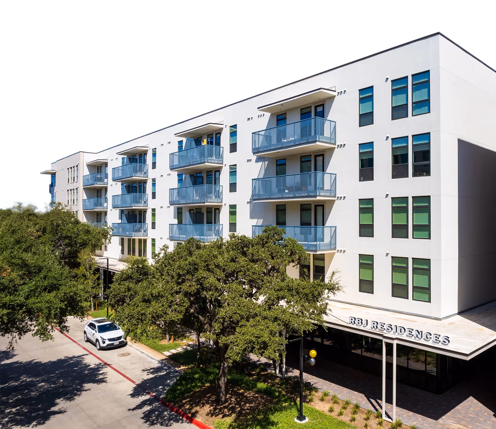 Exterior view of a white multi-story senior housing building with glass balconies and trees in front.