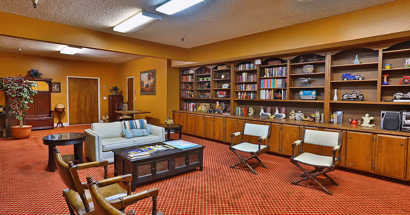 A cozy community lounge with seating, coffee tables, and a long built-in bookshelf along one wall.