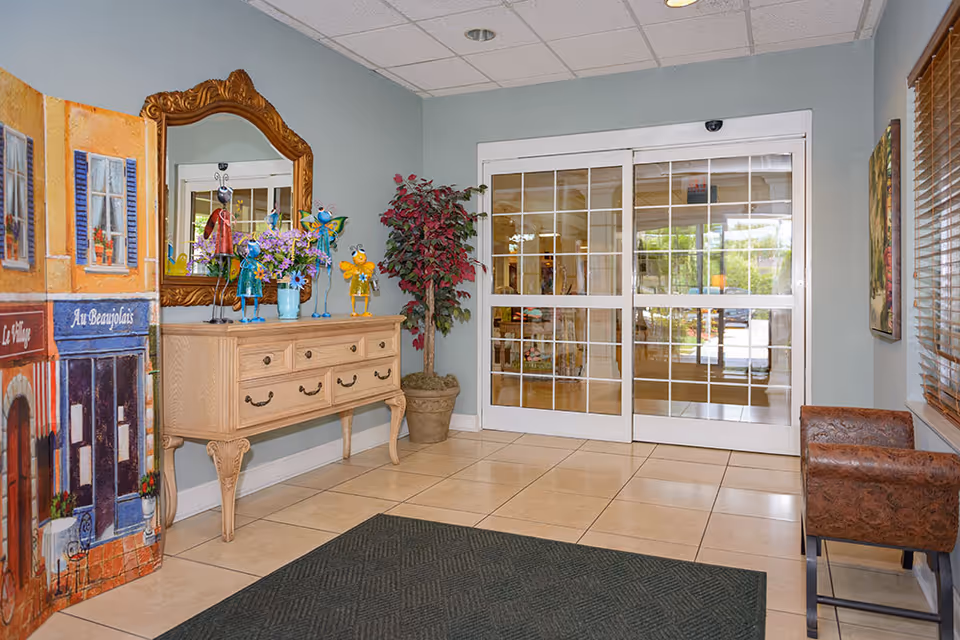 Interior lobby with glass sliding entrance doors, a decorative console table and mirror, potted plant, and seating area.