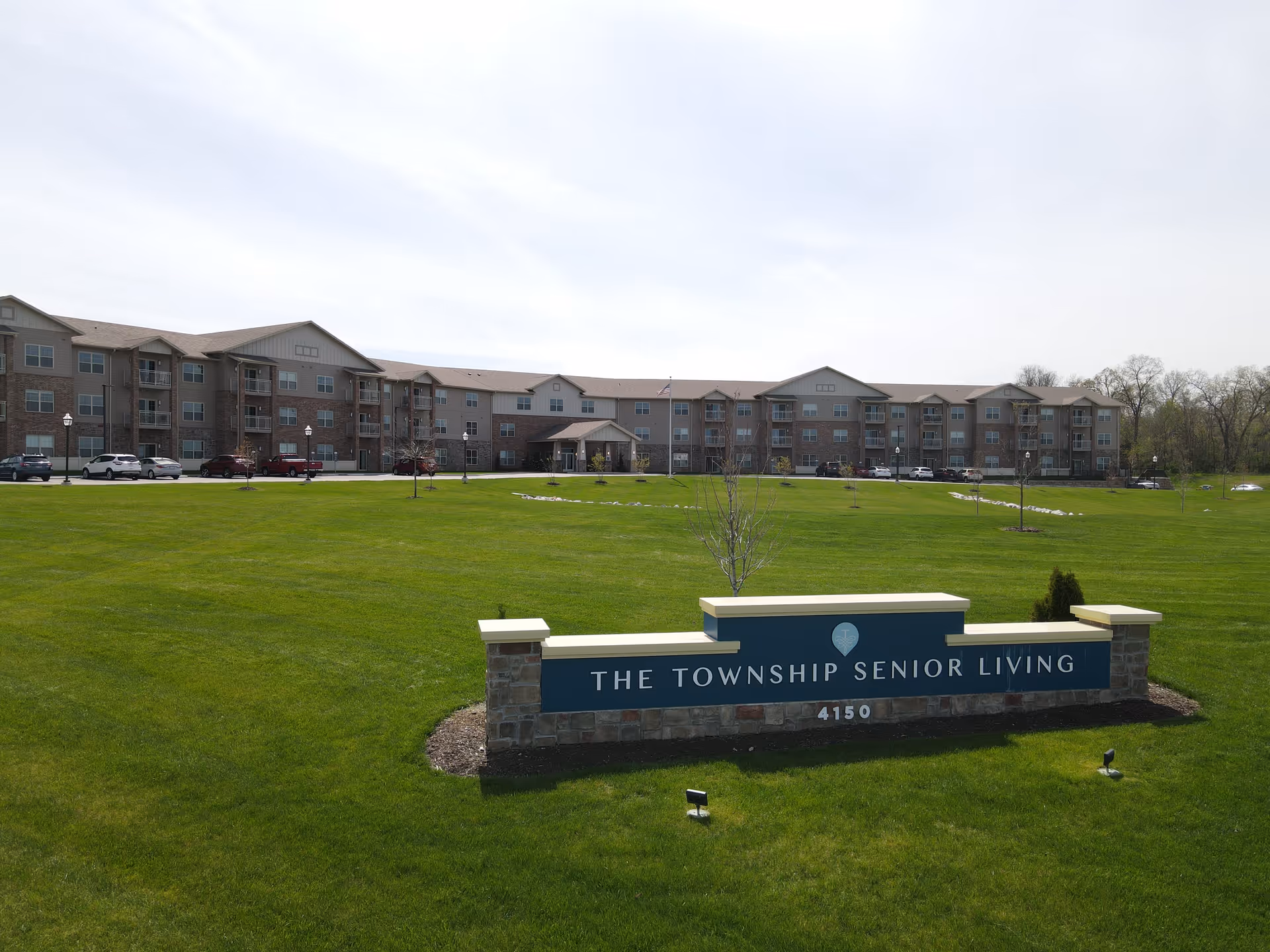 Front view of The Township Senior Living building with a large lawn and a stone sign reading 'The Township Senior Living'.