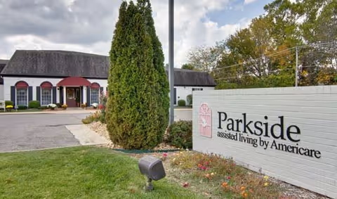 Entrance and landscaped front sign for Parkside assisted living by Americare with the facility building and driveway in view.