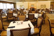 Spacious dining room with multiple round and rectangular tables set with napkins and upholstered chairs.