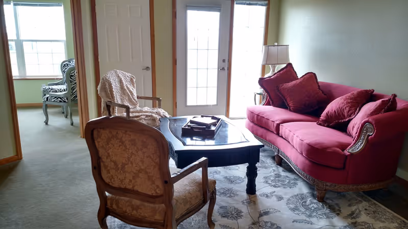 Cozy living room with a red upholstered sofa, patterned chairs, a coffee table, and a rug in front of glass doors.