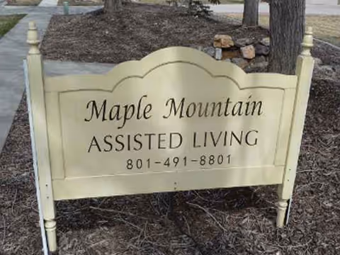 Exterior view of a cream Maple Mountain Assisted Living sign near trees.