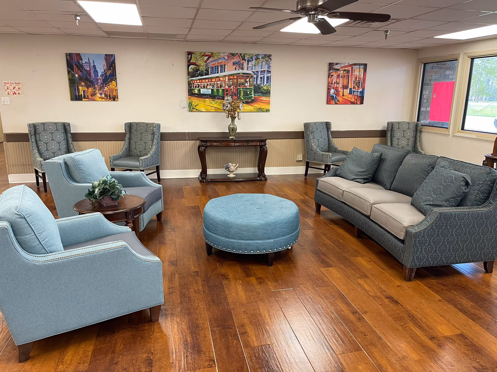 A bright lounge with sofas, armchairs, a round ottoman and wall art arranged on a wood floor.