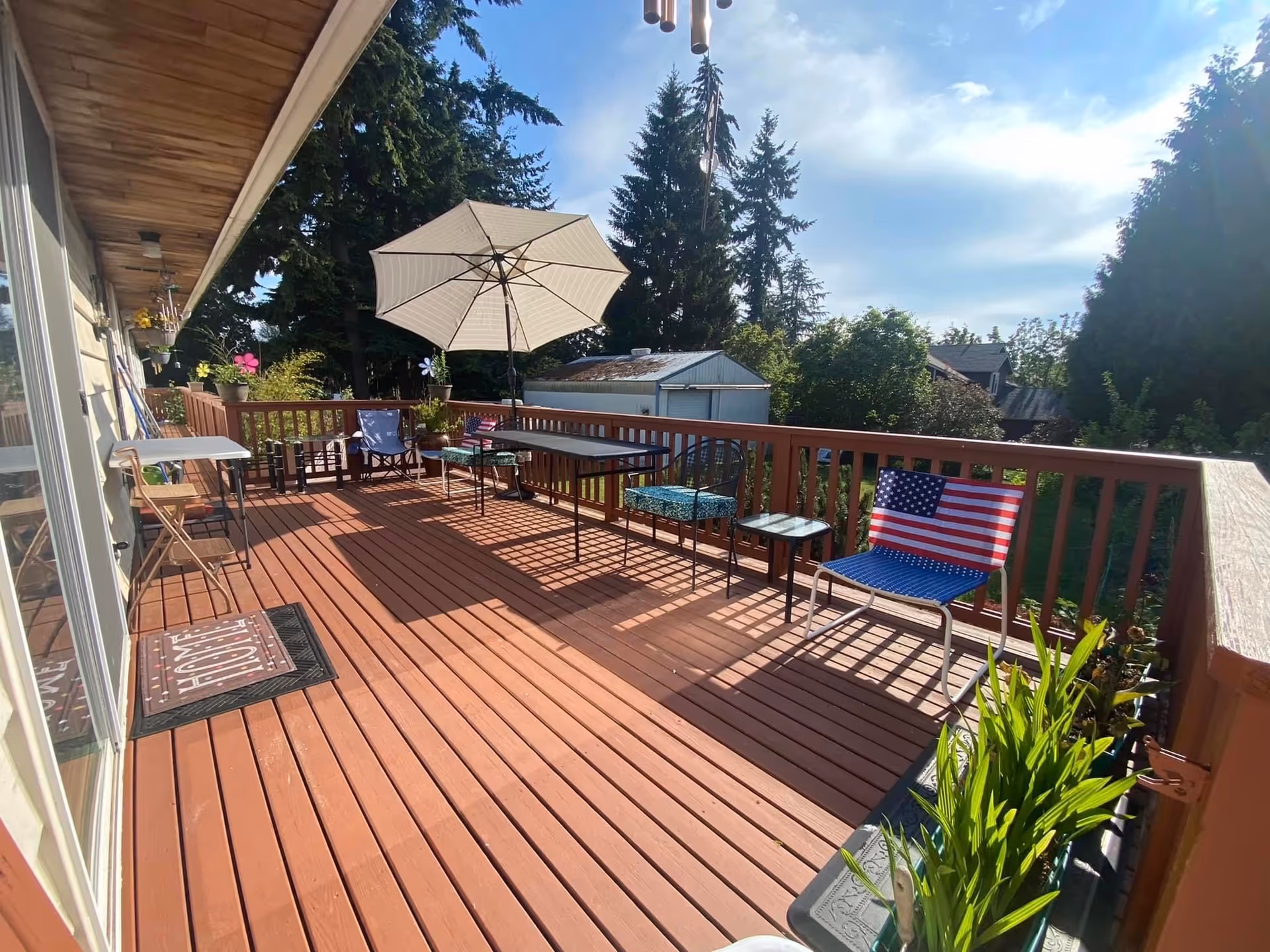 A deck area with chairs, a table, an umbrella, and greenery in the background.
