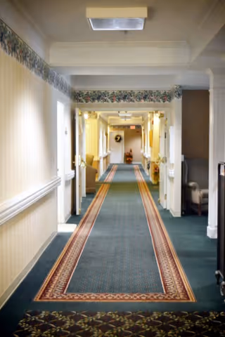 Long carpeted interior hallway with a patterned runner, doors and seating along the walls.