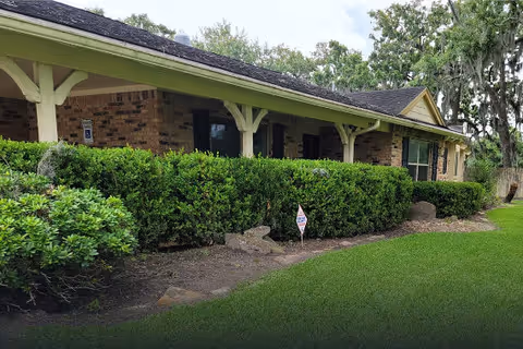 Single-story brick building with a covered porch, trimmed hedges and a manicured lawn in front.