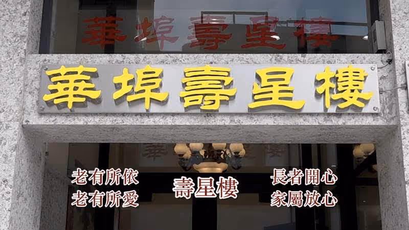 Entrance of East Bay Longevity Assisted Living 華埠壽星樓 with a stone frame and a signboard displaying the facility's name in large yellow Chinese characters. Additional Chinese text is visible below the sign, and a chandelier can be seen inside through the glass door.