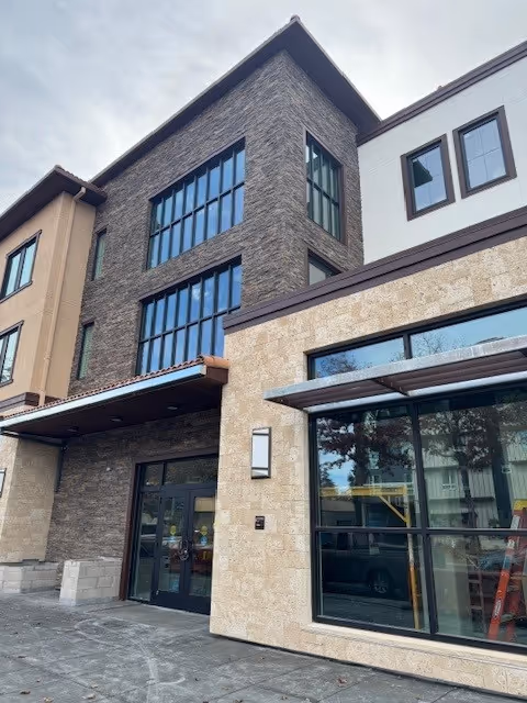 Front exterior of a multi-story memory care building with stone and stucco façade, large windows, and a ground-level entrance.