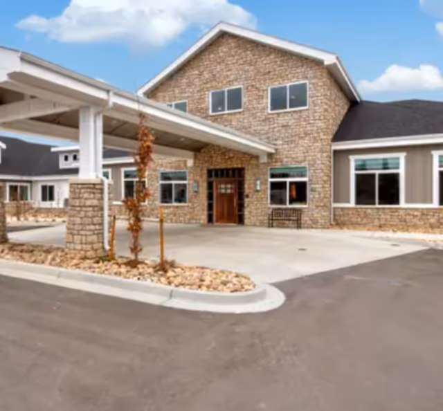 Exterior view of Greeley Village facility with brick facade, covered entrance, and driveway.