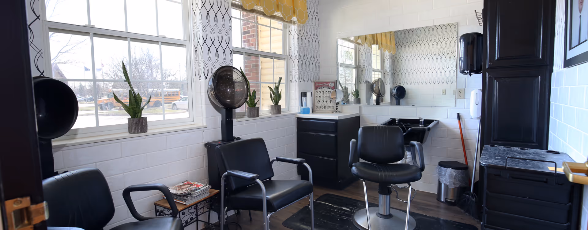 Small salon room with styling chairs, a hood dryer, sink, mirror, and storage cabinets.