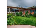 Landscaped green lawn and courtyard in front of a single-story brick care center with windows under a cloudy sky.