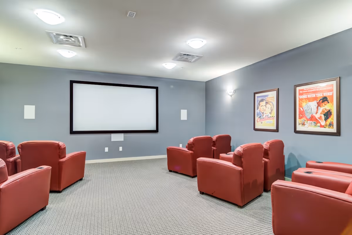 Small screening room with a blank projection screen, red recliner chairs and framed classic movie posters on the wall.