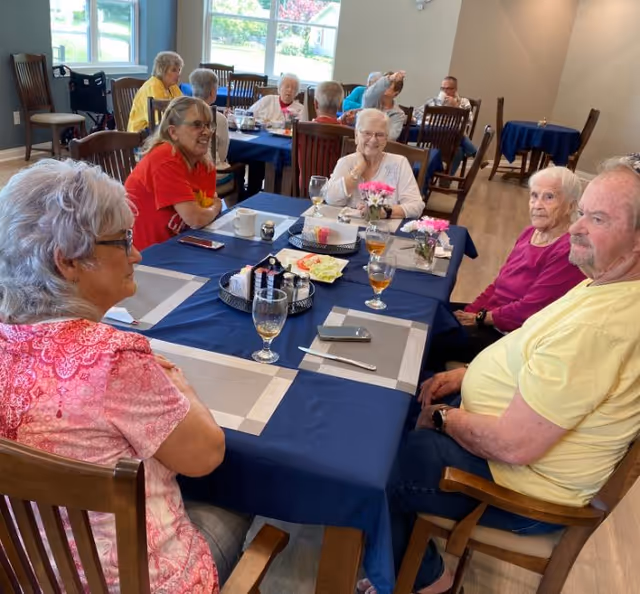 Several elderly residents seated around a table with place settings and drinks in a dining room.