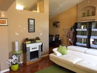 Bright living room with a white sectional sofa, decorative faux fireplace, green accents, and a view into a dining area.