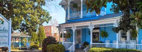 Blue Magnolia House exterior with a front porch and hanging plants.