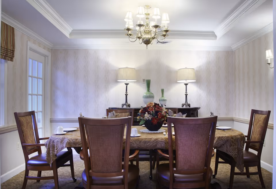 Formal dining room with a table set for six, a floral centerpiece, table linens, two lamps and a chandelier.