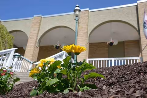 Exterior view of a brick senior living facility with arches and a blooming flower in foreground.