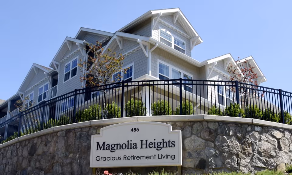 Exterior view of the Magnolia Heights retirement community building with its sign mounted on a stone wall in the foreground.