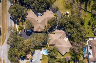 Aerial view of a residential area with multiple buildings surrounded by trees and greenery. There is a swimming pool visible near one of the buildings, and roads border the area on two sides.