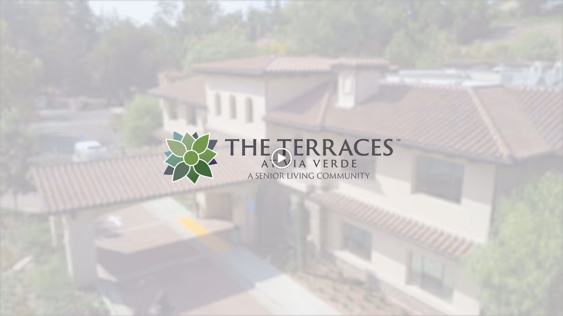 Exterior view of The Terraces at Via Verde senior living community building with a tiled roof and surrounding greenery.