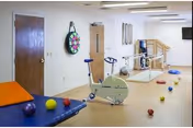 Indoor therapy/exercise room with a stationary bike, parallel bars, a therapy mat and scattered exercise balls.